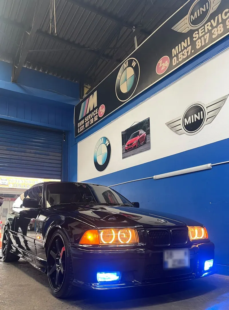 Blue M Servis atölyesinde BMW & MINI Service tabelasının altında duran siyah BMW 3 serisi